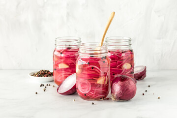 Jars of sliced pickled red onions with peppercorns and garlic cloves.
