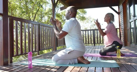 Focused senior african american couple practicing yoga on mats on sunny terrace, slow motion
