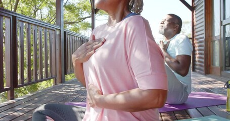 Focused senior african american couple practicing yoga on mats on sunny terrace, slow motion