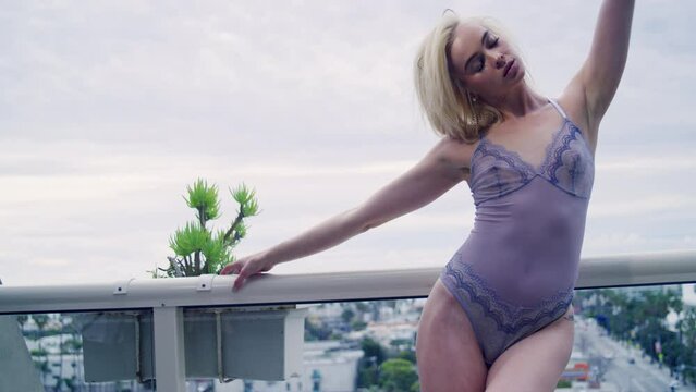 Woman in lingerie bodysuit stands on the balcony of a city hotel room 