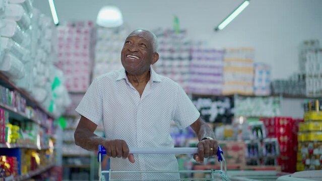 One joyful black Brazilian man pushing shopping cart at grocery store. African American consumer browsing for products to buy, looking at shelves