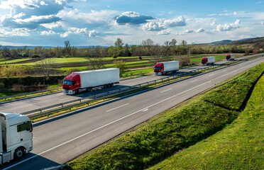 Highway transportation scene with Convoy of red and white transportation trucks in line on a rural highway under a beautiful blue sky