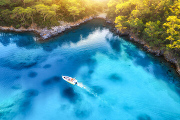 Speed boat on blue sea at sunrise in summer. Aerial view of motorboat in blue lagoon, rocks in clear azure water. Tropical landscape with yacht,  mountain with green forest. Top view. Oludeniz, Turkey - Powered by Adobe
