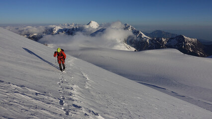 Naklejka na ściany i meble An alpinist is climbing the mountain (above the clouds). The assault on Kazbek