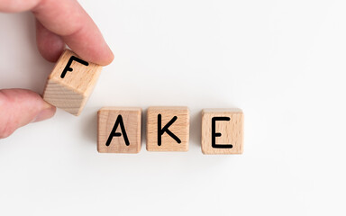 The word 'fake' written on wooden blocks, a man sitting in front of his desk with a pen and...