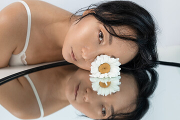 Close-up beautiful fresh face with daisy flower and water drops on skin. Beauty asian model with...
