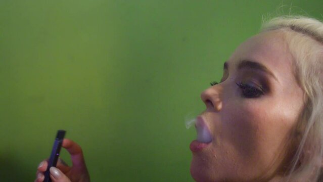 Woman smokes a vaporizer against a green wall