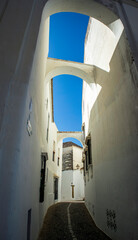 Vertical pictura of a narrow white alley of the old quarter of Arcos de la Frontera, Cadiz, Andalusia, Spain, with arches between the houses and blue sky © AntonioLopez