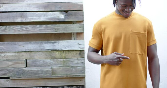 Happy african american man wearing yellow t shirt pointing to pocket, slow motion, copy space