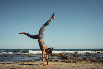 a beautiful brunette girl in gray leggings is engaged in fitness on the sand against the background of the sea