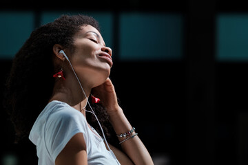 Relaxed black woman listening to music with headphones outdoors.