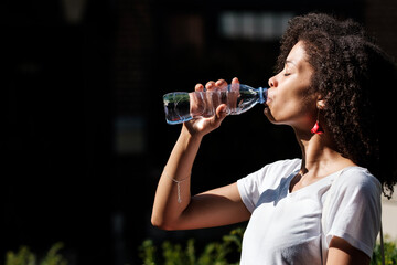 Attractive black woman drinking water from a bottle outside.