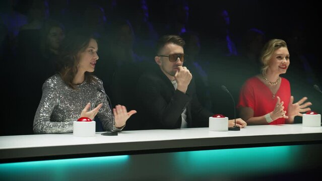 Portrait of celebrity judges enjoying the audition performed by talent on stage during the recording of a broadcast TV television talent show 