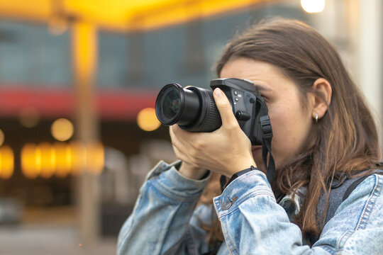 Close up of female photographer with professional camera covering her face taking photo in the city.