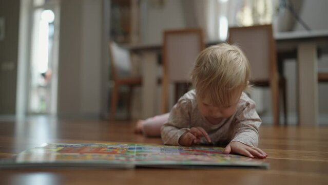 Little baby girl with a book. The child looks at a book with different pictures at home. 2 year old baby.