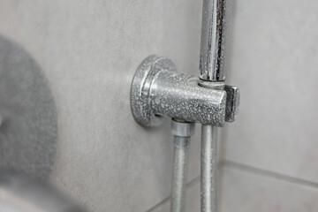Dirty calcified shower mixer tap, faucet with limescale on it, plaque from hard water, Chrome plated shower, close up photo. Bathroom with grey tiles interior.