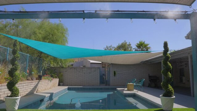 This slow motion video shows misters cooling a seating area that is overlooking someone's backyard pool.