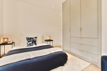 a bedroom with white walls and blue bedspremn in the bed is next to the cabinetd cupboards