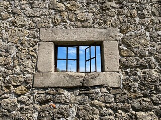Fototapeta na wymiar Old stone wall with a window through which you can see the blue sky