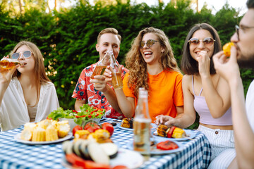 Cheerful young friends having at party outdoor, talking, drinking beer, and laughing enjoying at friendship. Vacation, picnic, weekend, nature.