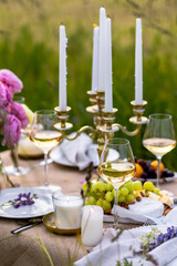 Summer sunset, romantic date outdoors in meadow, marriage proposal. Romantic sunset dinner in the field. Table honeymoon set for two with luxurious food, glasses of champagne drinks in a restaurant.
