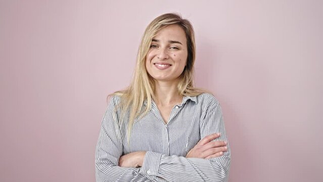 Young blonde woman smiling confident standing with arms crossed gesture over isolated pink background