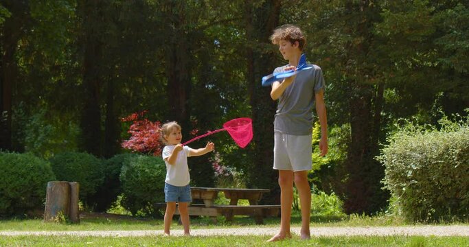 Baby with a red net plays with a teenager in a green park in summer. A little girl is playing with her bart, who is holding a blue toy airplane. Happy childhood in nature