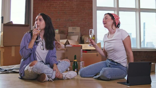 New roommates sit on the floor, drink wine and talk about how to decorate their urban apartment 