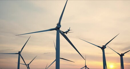 Large wind turbine rotating blades of in field against background of orange sunset on horizon with bright disk sun slow motion. Large passenger airplane, airliner landing at the airport runway. - Powered by Adobe