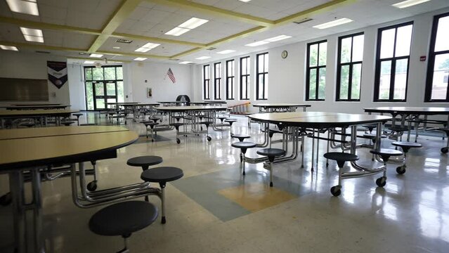 Trucking view to right showing dark and empty school cafeteria with tables and seats.