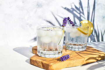 Chilled lavender lemonade with lemon and ice on a wooden stand on a gray table. Diet non-alcoholic...