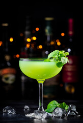 Last word alcohol cocktail drink with dry gin, herbal liqueur, lime juice and ice. Black bar counter background, steel bar tools and bottles