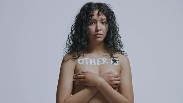 Mixed race woman with curly hair looks at the camera with the word Other painted on her bare chest