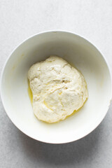 bread dough coated in olive oil, bread dough left to rise in white mixing bowl, process of making bread
