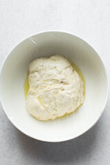 bread dough coated in olive oil, bread dough left to rise in white mixing bowl, process of making bread