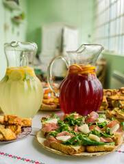 2 glass pitchers, one with lemonade, the other with sangria on a table with different delicacies