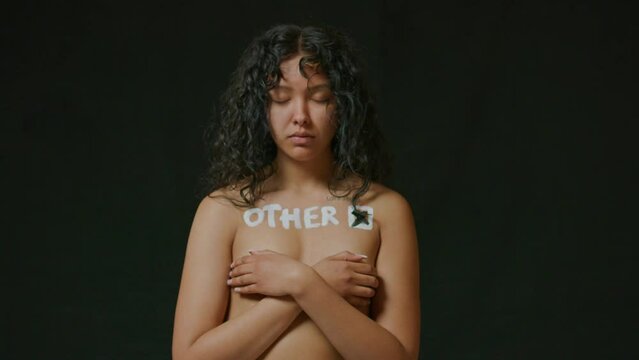 Hispanic woman looks up at the camera with Other painted on her bare chest
