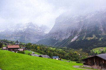 Grindelwald, Switzerland. Swiss Alps mountains landscape with fog. Photo with wooden chalet cottage on fresh green fields. 