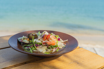 Spicy seafood salad, popular food on a wooden table, appetizing in a cafe next to the sea, Sue...