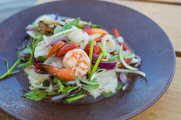 Spicy seafood salad, popular food on a wooden table, appetizing in a cafe next to the sea, Sue Flamingo, Ao Yon Beach, Phuket Thailand