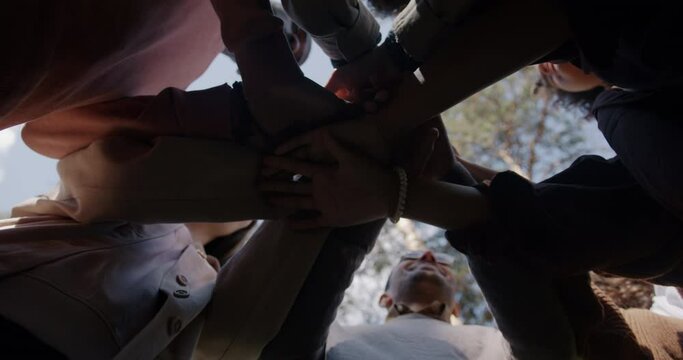 Low angle view of young people friends joining hands expressing unity outdoors in park against sky background. People and friendship concept.