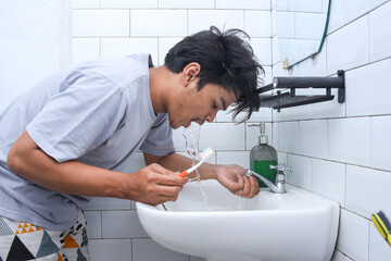Young man using water to clean his teeth and mouth after tooth brushing. Morning hygiene and activity concept. 