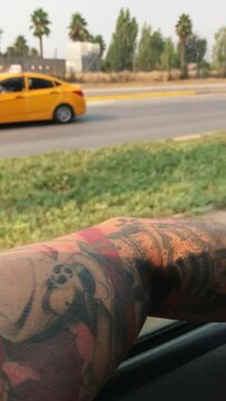 Serene road trip journey: the arm of a person with japanese tattoo resting on a car window, overlooking a scenic highway amidst nature