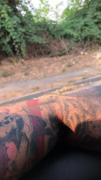 Serene road trip journey: the arm of a person with japanese tattoo resting on a car window, overlooking a scenic highway amidst nature