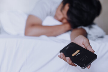 Young man is sleeping on the bed with the phone still in h is hand while the alarm ringing. Oversleeping concept. Selective focus - obrazy, fototapety, plakaty