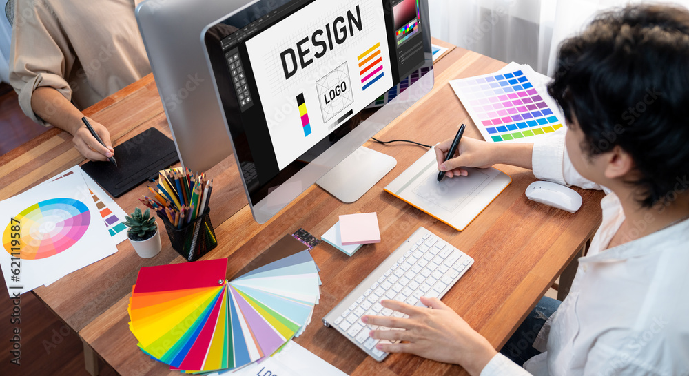 Poster Graphic designer work on computer laptop and with graphic drawing pen while brainstorming unique design with professional graphic team in modern digital studio workplace. Panorama shot. Scrutinize