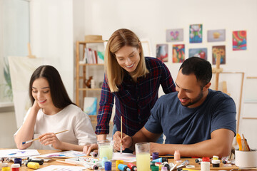 Fototapeta premium Artist teaching her students to paint at table in studio. Creative hobby