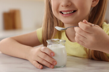 Cute little girl with tasty yogurt at white marble table indoors, closeup
