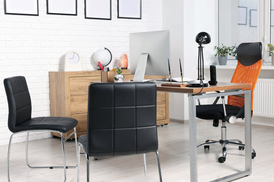 Stylish director's workplace with comfortable desk, computer and chairs for visitors in office. Interior design