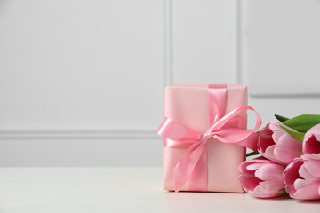 Beautiful gift box with bow and pink tulips on white table. Space for text